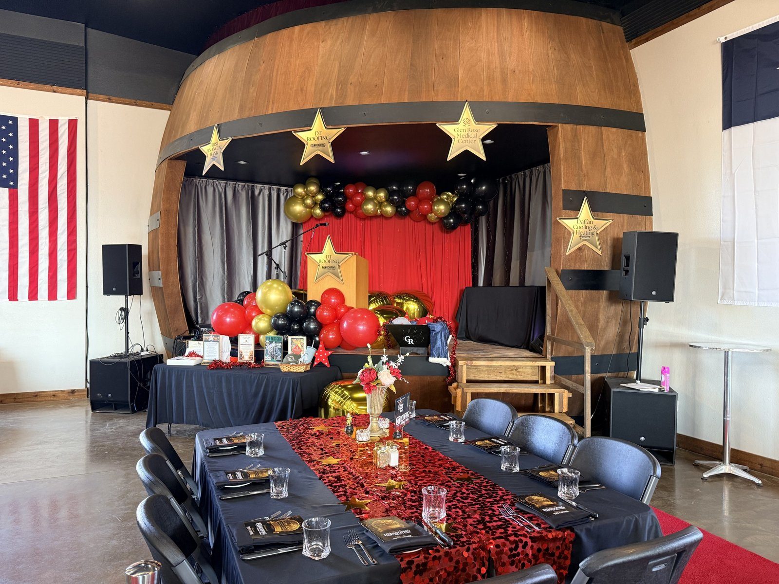 Corporate retreats in Texas at Twin Canyons Ranch: the whiskey-barrel stage inside the Black Star Barn set for an event, with a red curtain, balloon garland and a long dressed table