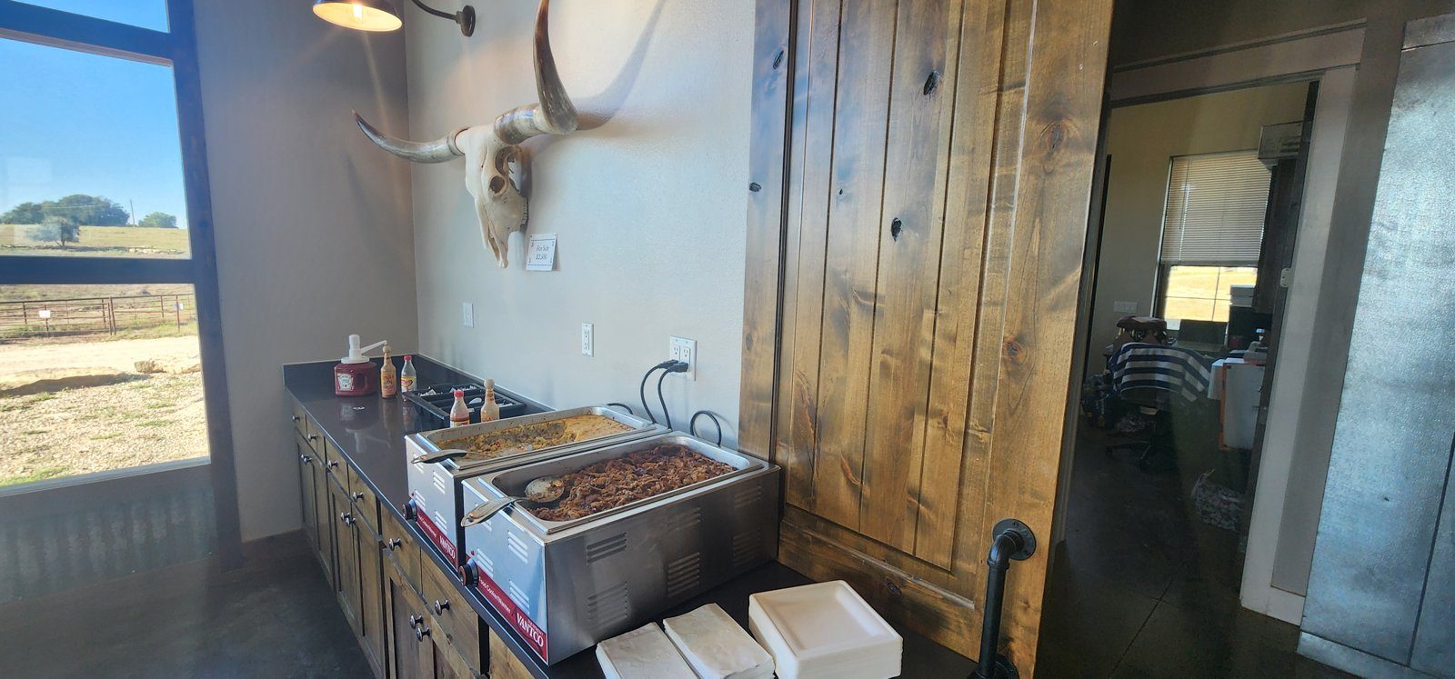 A buffet line of covered chafing dishes along a wood-paneled wall, with a Longhorn skull mounted above