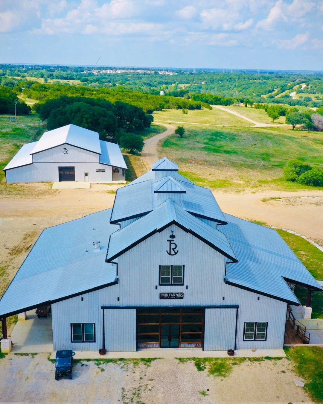 Aerial view of the white Black Star Barn with its metal roof, a smaller white building behind it and green pasture beyond