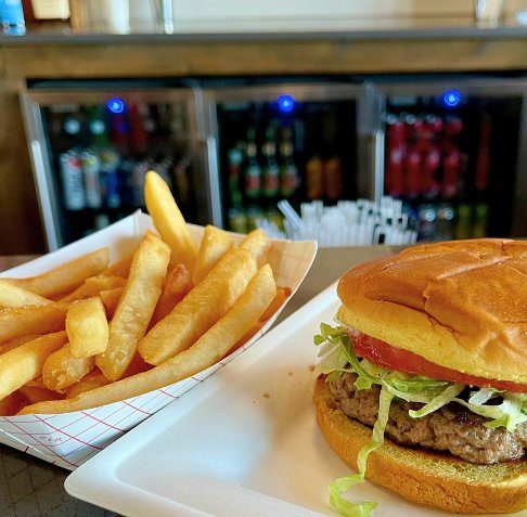 A burger with lettuce and tomato beside a basket of fries on a white plate at the bar