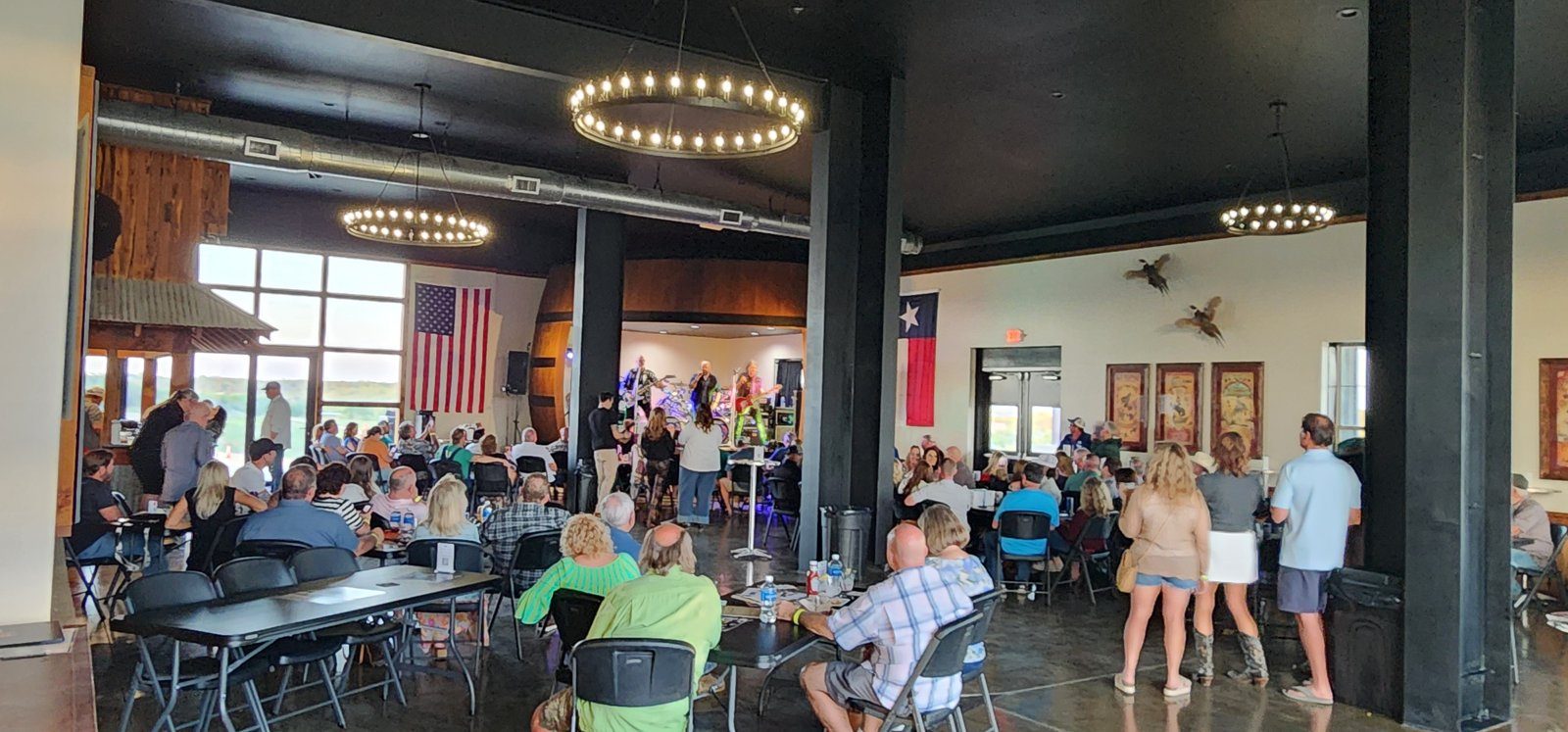 A Friday crowd at one of the live music venues in Texas: tables inside the Black Star Barn under ring chandeliers, with American and Texas flags on the walls