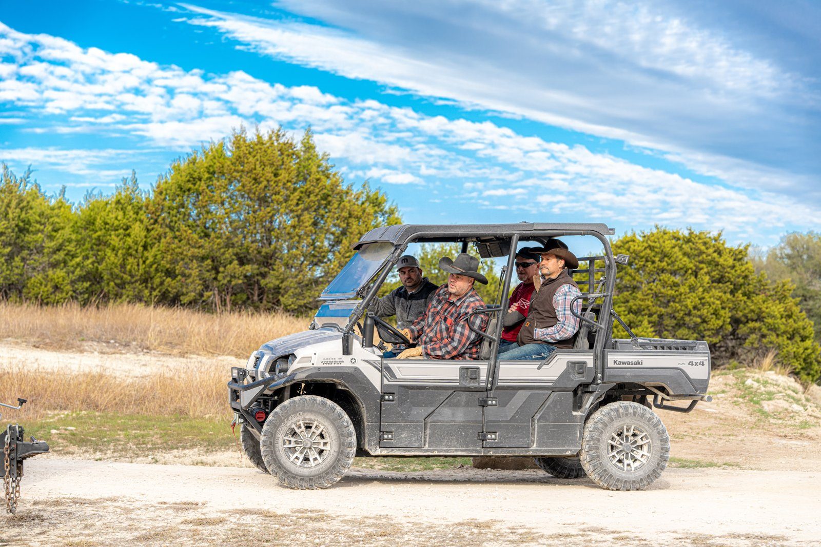 Team building in Texas on a UTV ranch tour: a UTV with riders on a gravel ranch road under a blue sky with clouds and brush behind it