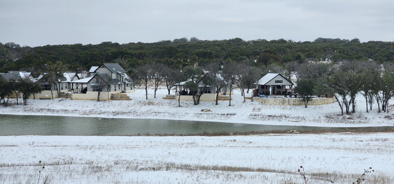A Texas ranch getaway in winter: villas across a pond on a snowy winter day, with snow covering the ground and the banks